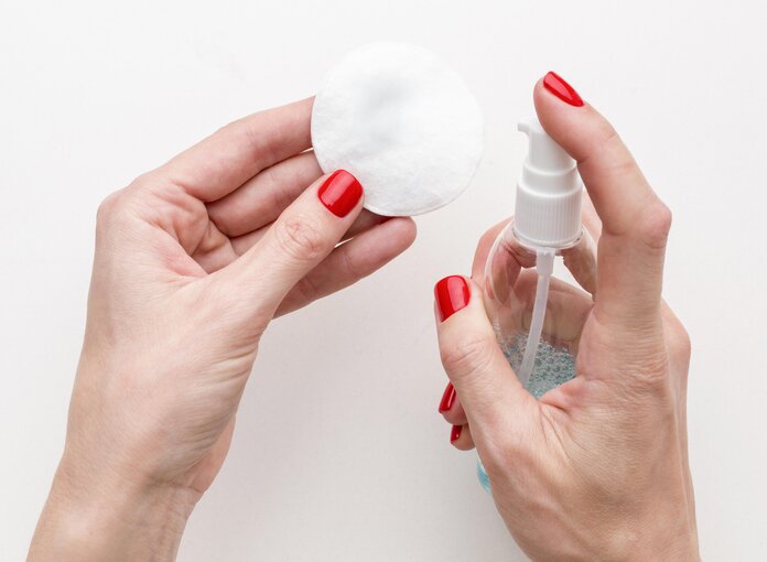 Nagellack Entfernung, © freepik Hände mit lackierten Nägeln besprühen ein Kosmetikpad mit einer Sprühflasche.