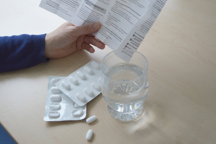 Beipackzettel von Medikamenten lesen, © Krebsinformationsdienst, DKFZ Eine Hand hält eine Packungsbeilage, davor liegen Tabletten auf den Tisch sowie ein Glas Wasser.