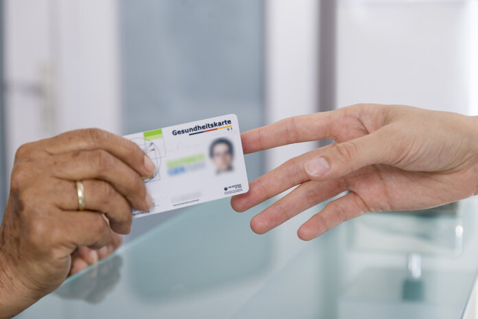 Versichertenkarte, © Krebsinformationsdienst, DKFZ; Foto: Tobias Schwerdt Eine Hand reicht einer anderen eine Versichertenkarte (Gesundheitskarte).