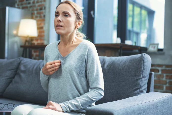 Hitzewallungen in den Wechseljahren, © yacobchuck, Thinkstock Frau mit einem angestrengtem Blick sitzt in einem verschwitzten T-Shirt auf dem Sofa.