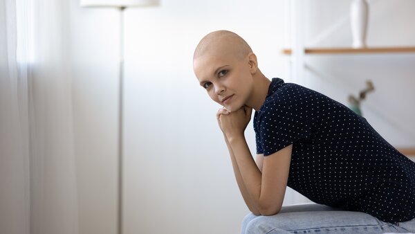 Junge nachdenkliche Patientin mit Glatze stützt ihren Kopf auf die Hände.