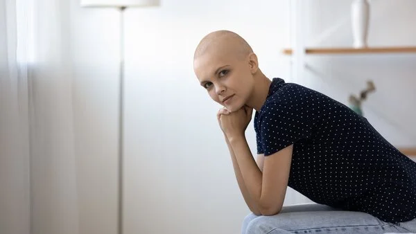 Junge nachdenkliche Patientin mit Glatze stützt ihren Kopf auf die Hände.