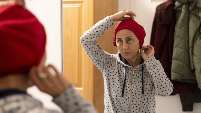Frau probiert vor dem Spiegel eine Mütze auf, © Krebsinformationsdienst, DKFZ; Foto: Tobias Schwerdt Eine Frau probiert vor dem Spiegel eine Mütze auf. Man sieht keine Kopfhaare.