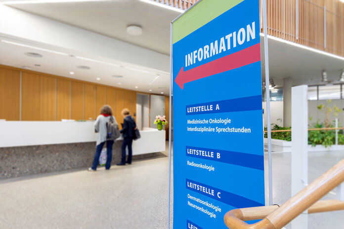 Informationstafel, © Krebsinformationsdienst, DKFZ; Foto: Tobias Schwerdt Eingangsbereich Krankenhaus mit Informationstafel und Personen.
