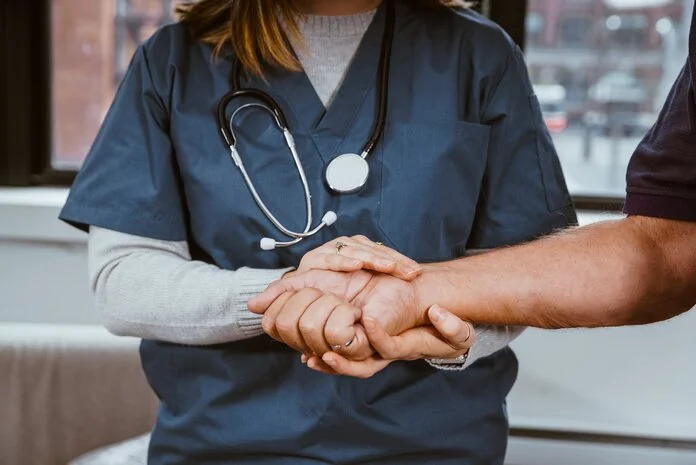 Unterstützung, © Nicole De Khors, Burst Pflegerin hält die Hand eines Patienten.