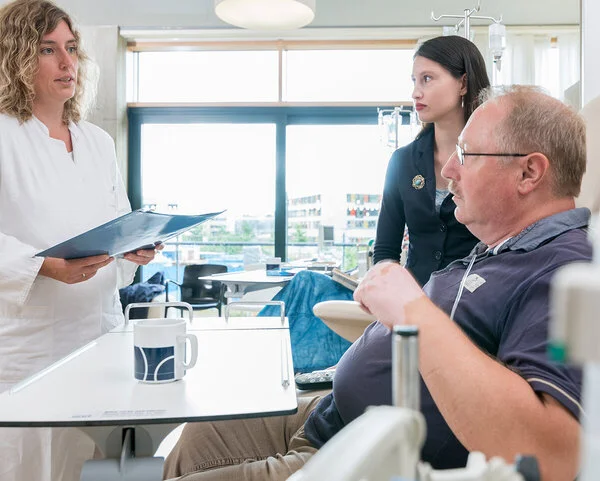 Krebsbehandlung, Foto: Tobias Schwerdt © Krebsinformationsdienst, DKFZ Ärztin steht vor dem Krankenbett eines Patienten mit seiner Angehörigen und spricht über die weitere Behandlung.