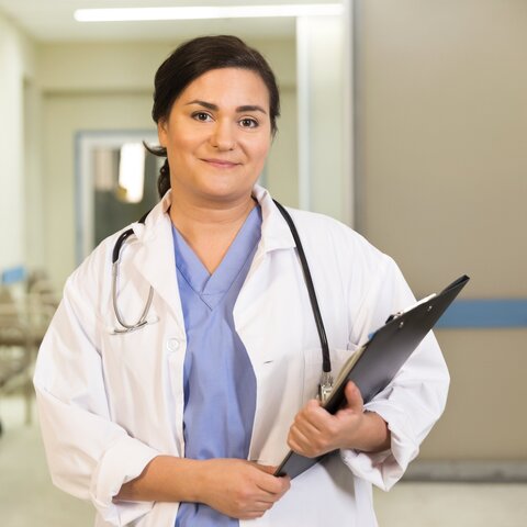 Ärztin steht im im Krankenhausflur mit Clipboard in der Hand
