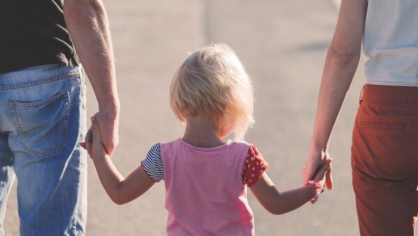 Ein kleines Kind läuft Hand in Hand mit seinen Eltern.