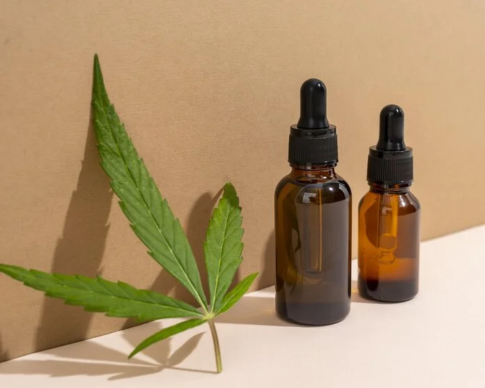 CBD-Öl neben Hanfblatt, © Freepik wei braune Glasfläschchen mit Pipette stehen neben einem grünen Hanfblatt.