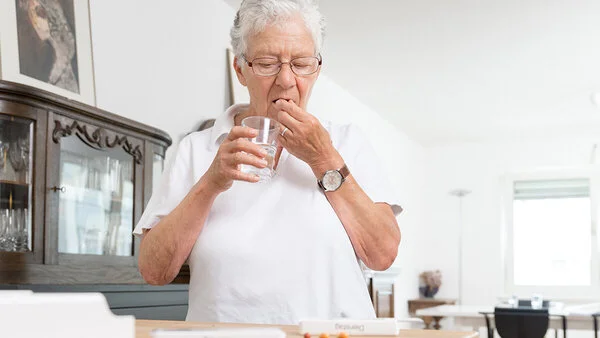 Medikamenteneinnahme, Bild: Tobias Schwerdt Ältere Dame nimmt Medikamente mit einem Glas Wasser ein.