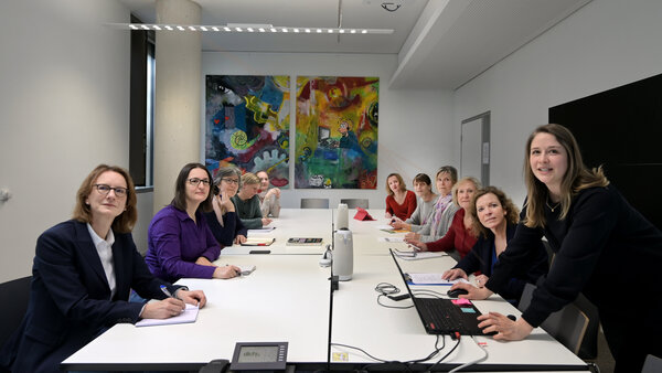 Mitarbeiterinnen des Krebsinformationsdienstes sitzen an einem Besprechungstisch und hören bei einer Präsentation einer Kollegin zu.