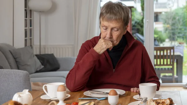 Kein Appetit, © Krebsinformationsdienst, DKFZ; Foto: Tobias Schwerdt Eine ältere Frau sitzt ohne Appetit an einem Esstisch mit Frühstück.