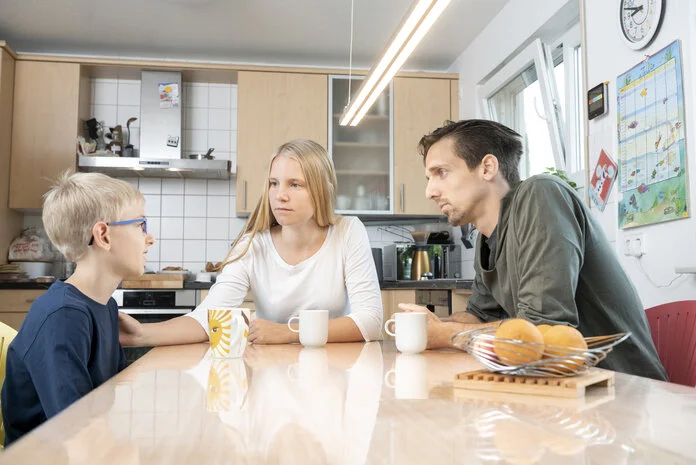 Eine junge Frau und ein Mann sitzen im Gespräch mit einem Kind am Tisch