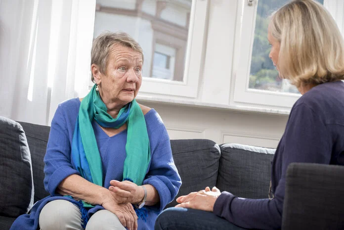 Psychoonkologischen Beratung , © Krebsinformationsdienst, DKFZ; Foto: Tobias Schwerdt Ältere Frau mit kurzen grauen Haaren sitzt auf einer grauen Couch und unterhält sich mit einer jungen Frau mit blondem schulterlangem Haar.