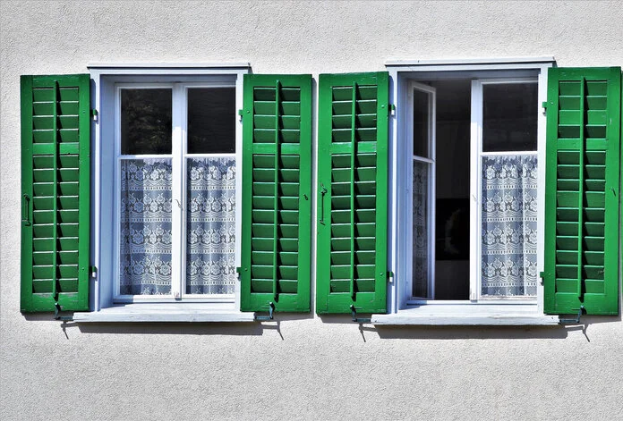 Zwei Fenster mit grünen Fensterläden, ein Fenster ist zum Lüften geöffnet.
