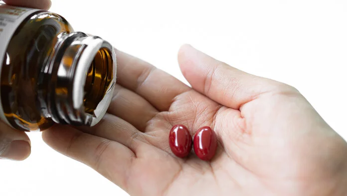 Nahrungsergänzungsmittel , © wing-wing, iStock Nahaufnahme: Eine Frau schüttet sich 2 rote Kapseln aus einer braunen Flasche auf die ausgestreckte Handfläche.