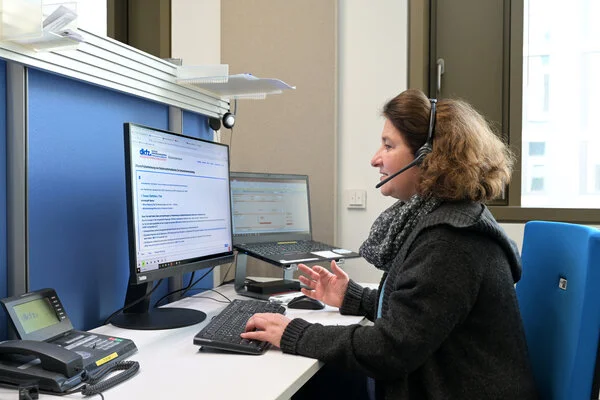 Ärztin bei der Arbeit im Telefondienst, © Krebsinformationsdienst, DKFZ; Foto: Klaus Landry Eine Ärztin vom Telefondienst des Krebsinformationsdienstes sitzt an einem Arbeitsplatz mit 2 Computer-Bildschirmen, auf die sie schaut, während sie über ein Headset telefoniert.