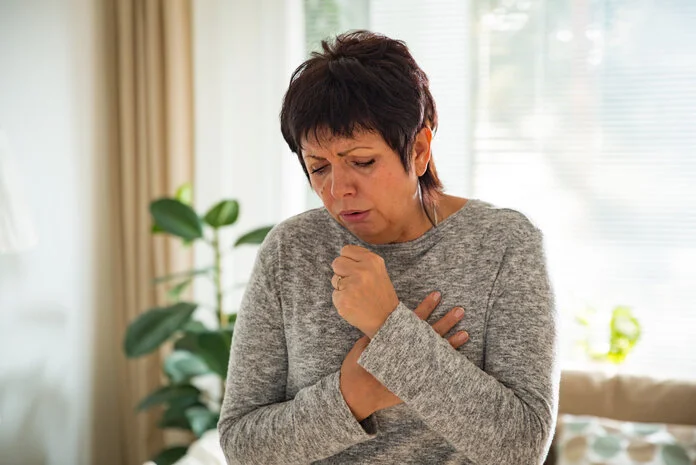 Husten, © Aleksandra Suzi, Shutterstock Eine Frau mit kurzen Haaren hustet in ihre Hand.