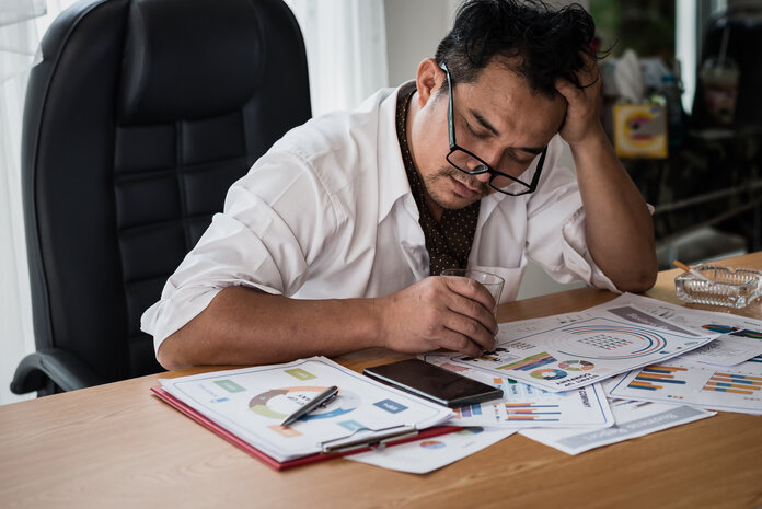 Gestresster Mann, © worawit_j - shutterstock Gestresster Mann am Schreibtisch mit Alkohol und Zigaretten