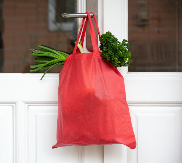 Einkaufstasche, © Maren Winter, Shutterstock Eine rote Tasche mit Lebensmitteleinkäufen hängt an einer Tür.