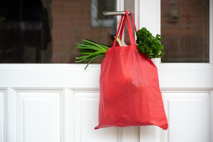 Einkaufstasche, © Maren Winter, Shutterstock Eine rote Tasche mit Lebensmitteleinkäufen hängt an einer Tür.