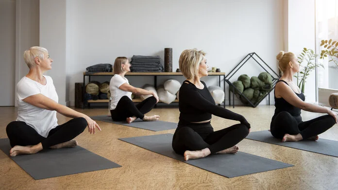 Eine Gruppe von Frauen sitzen auf ihrer Sportmatte in Yoga-Haltung.