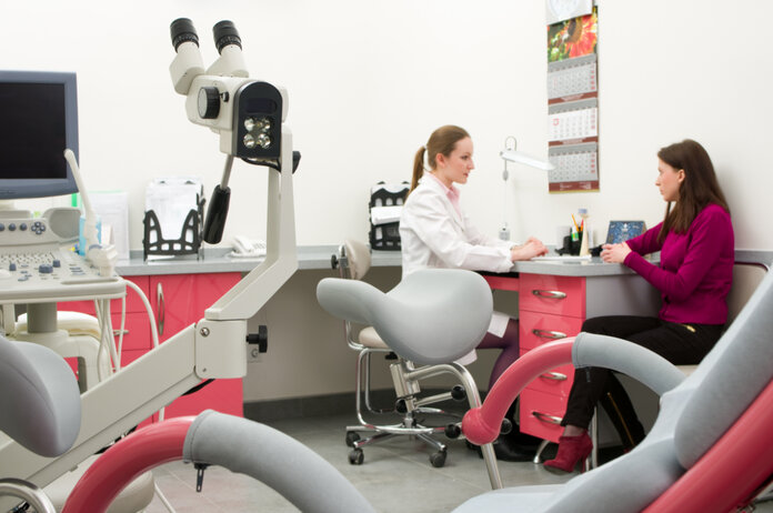 Besuch bei der Frauenärztin Frauenärztin spricht mit einer Patientin; im Vordergrund ein Gynäkologiestuhl
