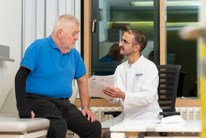 Arzt-Patienten-Gespräch, © Krebsinformationsdienst, DKFZ; Foto: Tobias Schwerdt Ein Arzt erklärt einem älteren Mann, der auf einer Untersuchungsliege sitzt, seinen Befund.