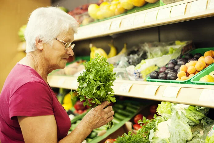 Lebensmittel-Einkauf, © gpointstudio, Thinkstock Seniorin steht vor einer Gemüsetheke und hält einen einen Strauß Kräuter in der Hand