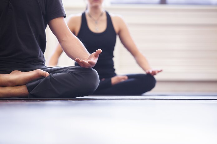 Yoga, © ZephyrMedia, Shutterstock Zwei Personen sitzen im Schneidersitz
