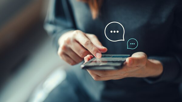 Finger einer Frau wischen über ein Smartphone, eingeblendet sind Chat-Sprechblasen.