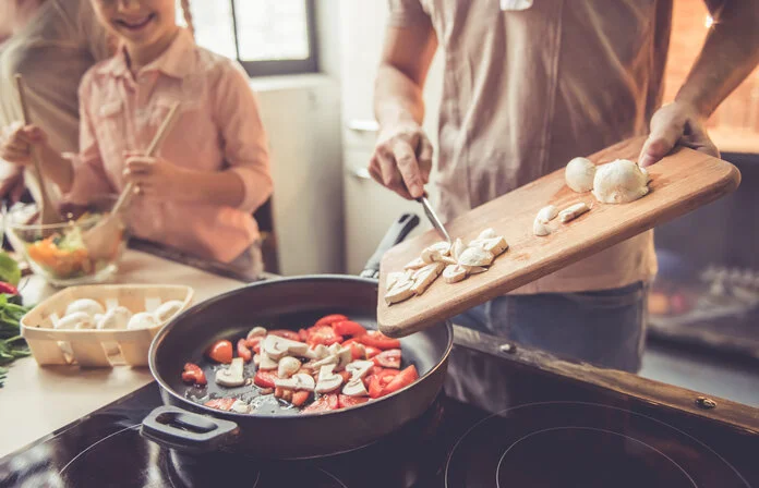 Gesund kochen, © George Rudy, Shutterstock Mann steht vor einer Pfanne und gibt geschnittenes Gemüse dazu.