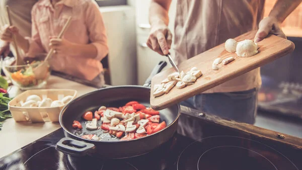 Gesund kochen, © George Rudy, Shutterstock Mann steht vor einer Pfanne und gibt geschnittenes Gemüse dazu.