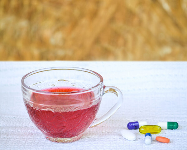 Neben einer Tasse Tee liegen verschiedene Kapseln und Tabletten.