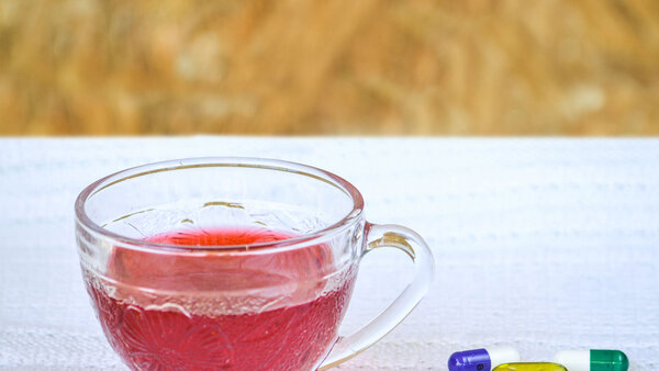 Neben einer Tasse Tee liegen verschiedene Kapseln und Tabletten.