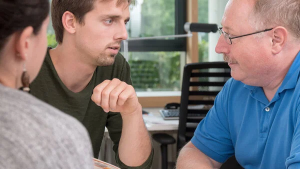 Beratungsgespräch, © Krebsinformationsdienst, DKFZ; Foto: Tobias Schwerdt Ein junger Mann und ein älterer Mann halten eine Broschüre und sprechen mit einer Frau.