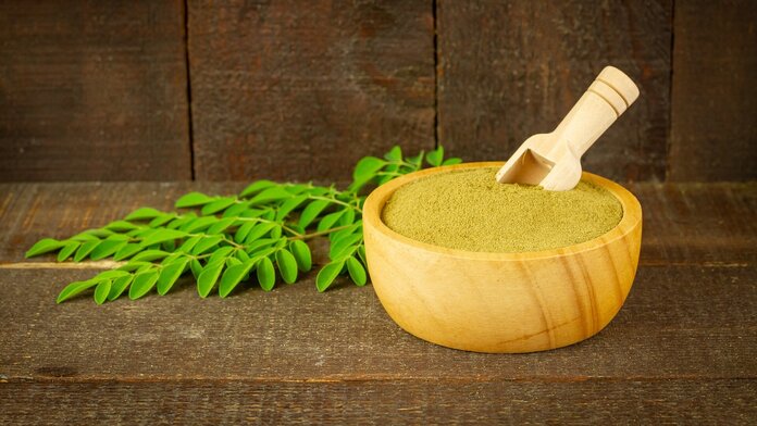 Moringa-Blätter an einem Zweig und Moringa-Pulver in einer Schüssel.