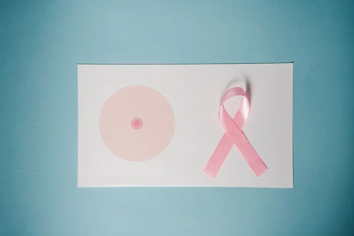 Symbolbild Mastektomie, © Klaus Nielsen, Pexels Symbolische Darstellung einer Mastektomie: Auf einem waagerechten Blatt Papier, das mit einer vereinfachten weiblichen Brust bedruckt ist, liegt eine pinke Awareness-Schleife an der Stelle, an der die zweite Brust sein sollte.