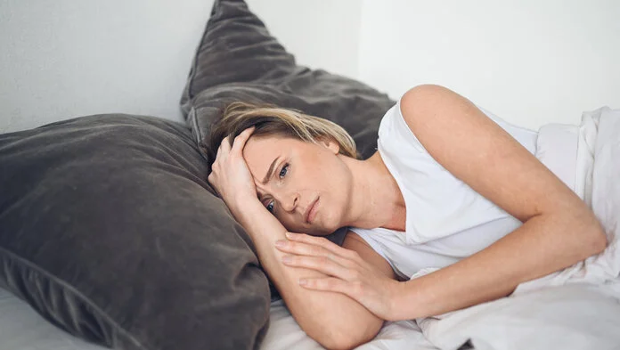 Schlafstörungen bei Krebs, © user14699452, Freepik Junge Frau liegt im Bett und hält sich erschöpft den Kopf.