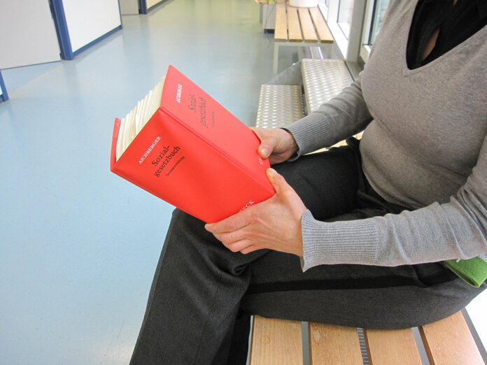Sozialgesetzbuch, © Krebsinformationsdienst, DKFZ Hände halten das rote Sozialgesetzbuch.