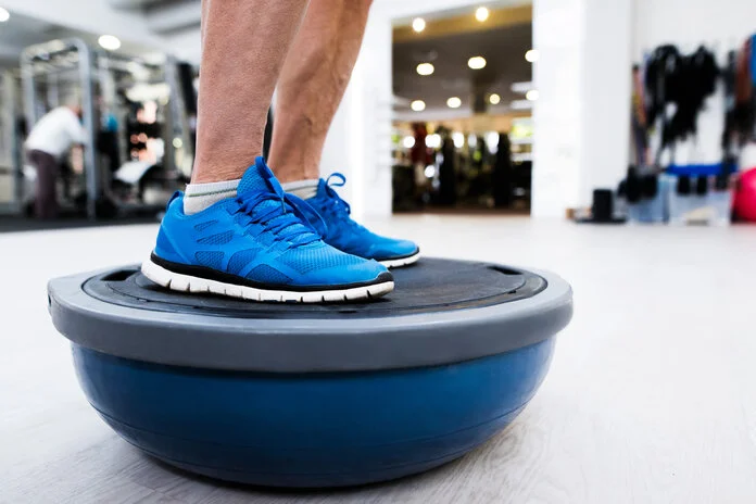 Balanceübungen , © Halfpoint - Thinkstock Eine Person macht Balanceübungen auf einem halbierten Ball im Trainingsraum der Physiotherapie.