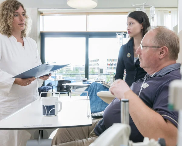 Arztgespräch, © Krebsinformationsdienst, DKFZ; Foto: Tobias Schwerdt Ärztin spricht mit Patient und einer jungen Angehörigen, während der Patient ambulant eine Infusion erhält.