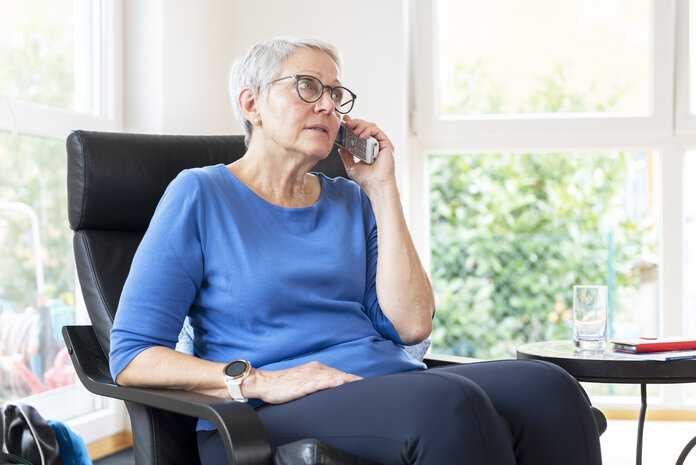 Ältere Frau sitzt in einem Sessel und telefoniert.