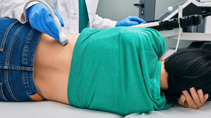 Eine Frau liegt auf der Seite, während eine Ärztin ihre Niere mit einem Ultraschallgerät untersucht.