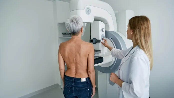 Ältere frau bei Mammographie, © Peakstock, Shutterstock Eine ältere Frau steht oberkörperfrei vor einem Mammographie-Gerät, neben ihr steht eine Röntgenassistentin.