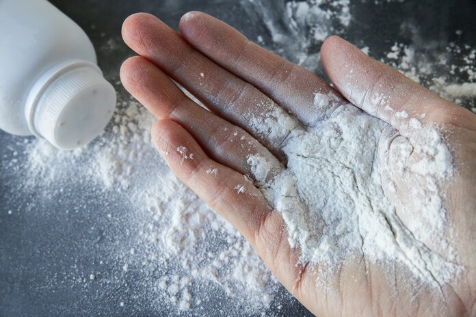 Auf einer Hand liegt Talkumpuder, darunter eine umgefallene Puderdose und Talkumpuder zerstreut