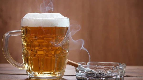 Alkohol und Tabak, © Lecic - thinkstock.com Volles Bierglas steht auf einem Tisch neben einem Aschenbecher mit einer qualmenden Zigarette