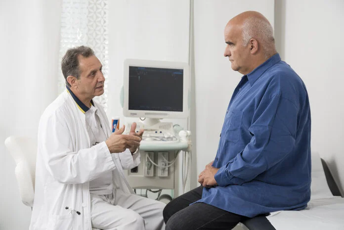 Arztgespräch nach Ultraschalluntersuchung, © Krebsinformationsdienst, DKFZ; Foto: Tobias Schwerdt Älterer Mann sitzt auf einem Untersuchungstisch in einer Arztpraxis und spricht mit seinem Arzt nach einer Ultraschalluntersuchung.