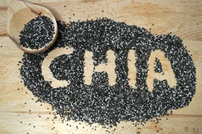 Chia-Samen, flaviuz/Fotolia Chia-Samen liegen auf einem Holztisch, das Wort "Chia" wurde mit dem Finger in den Haufen Chia-Samen geschrieben.